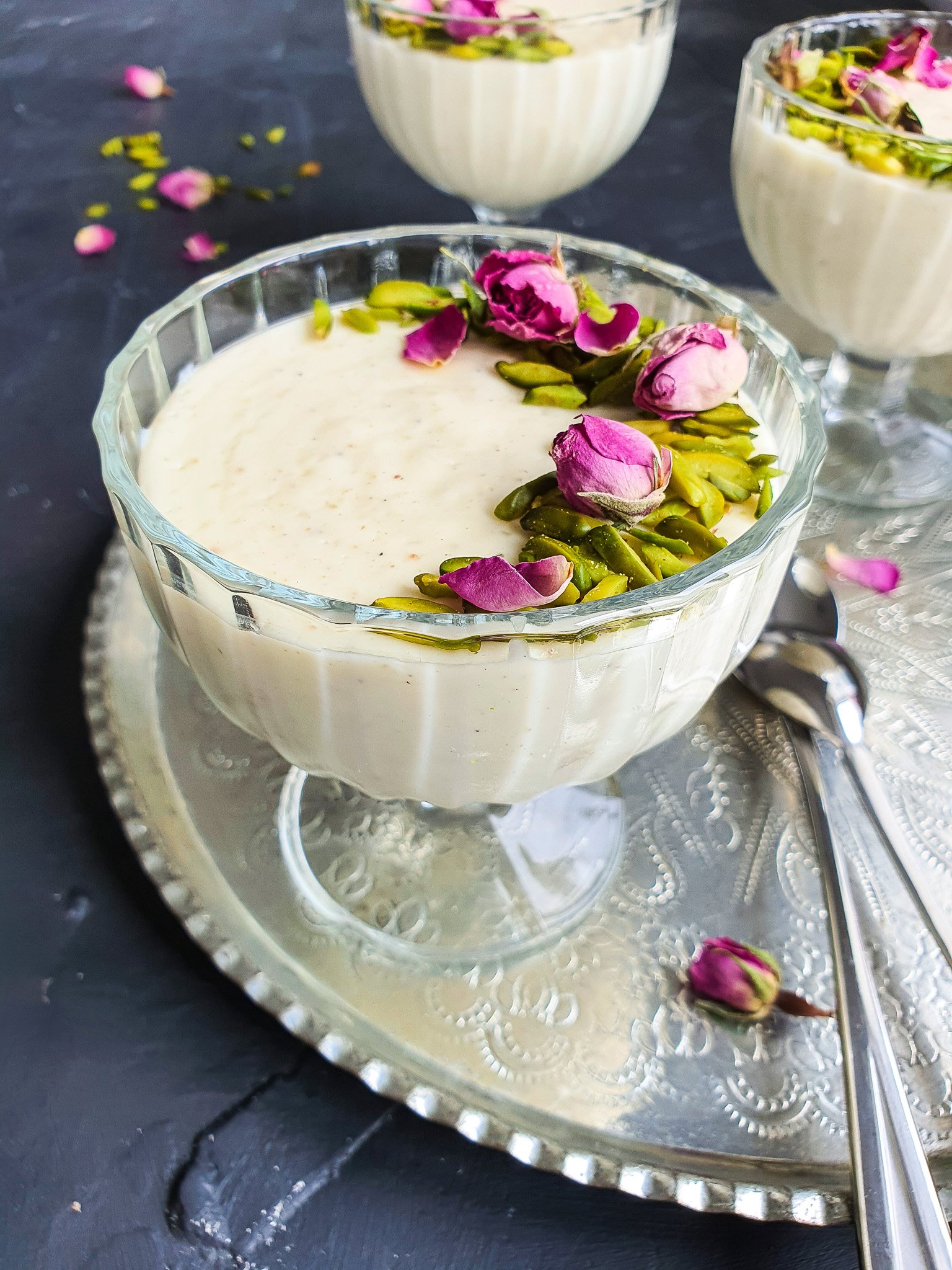 Muhallebi (Muhalabia) Middle Eastern Milk Pudding in a ice cream dish with a spoon, garnished with pistachios and rose petals 