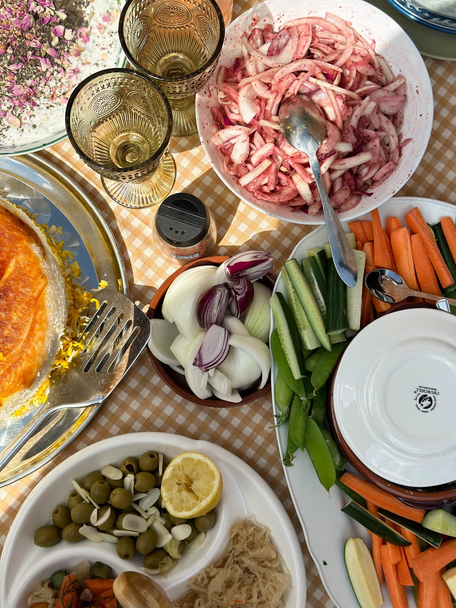 A vibrant family spread at a Persian manghal party, featuring a variety of dishes including kababs, rice, salads, and an array of colorful side dishes, set on an outdoor table.