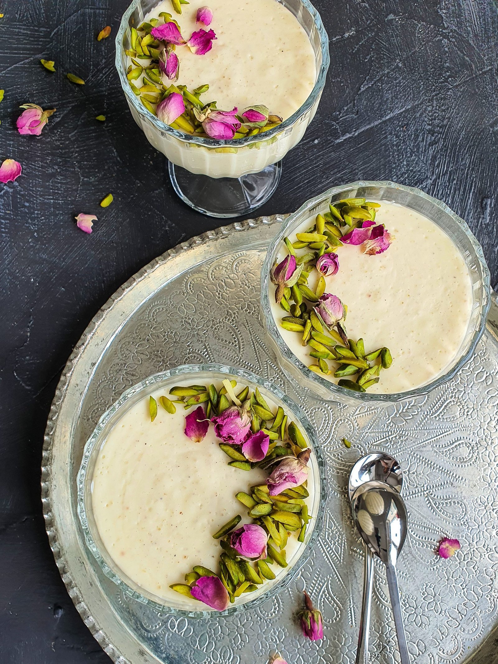 A bowl of creamy Muhallebi (Muhalabia) Middle Eastern Milk Pudding with a sprinkle of green pistachios and pink rose petals on top.