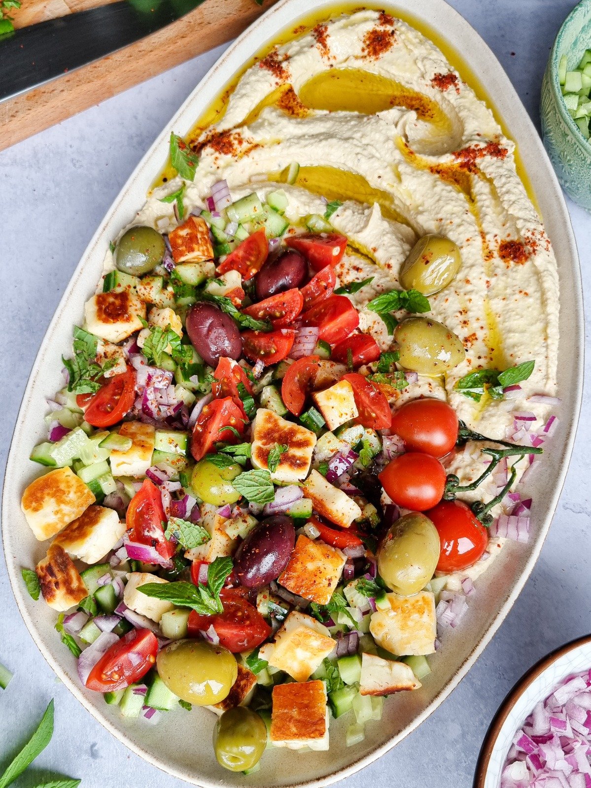 A dish of hummus topped with veggies and grilled halloumi