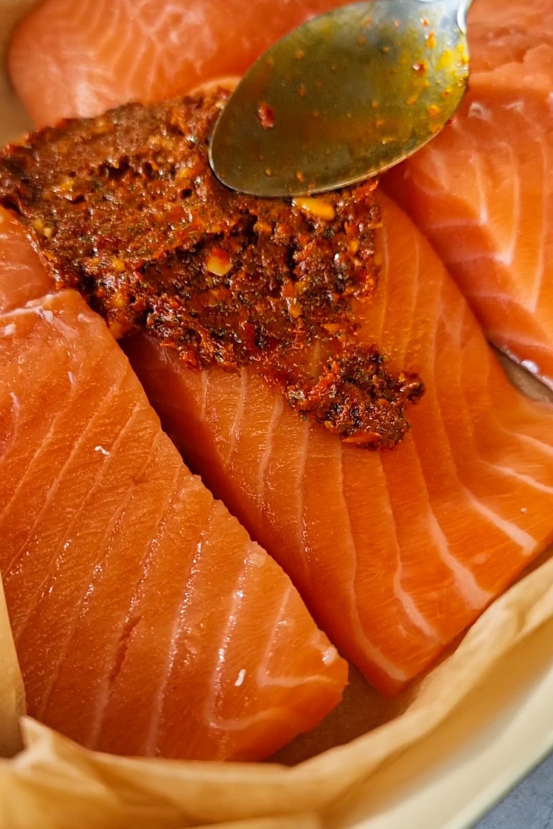 Start by mixing the oil with minced garlic, sweet pepper paste and all the spices, dried dill, pup biber, turmeric, black pepper and salt to form a paste.  Line up the salmon on a baking tray and spread the paste on top of the salmon.