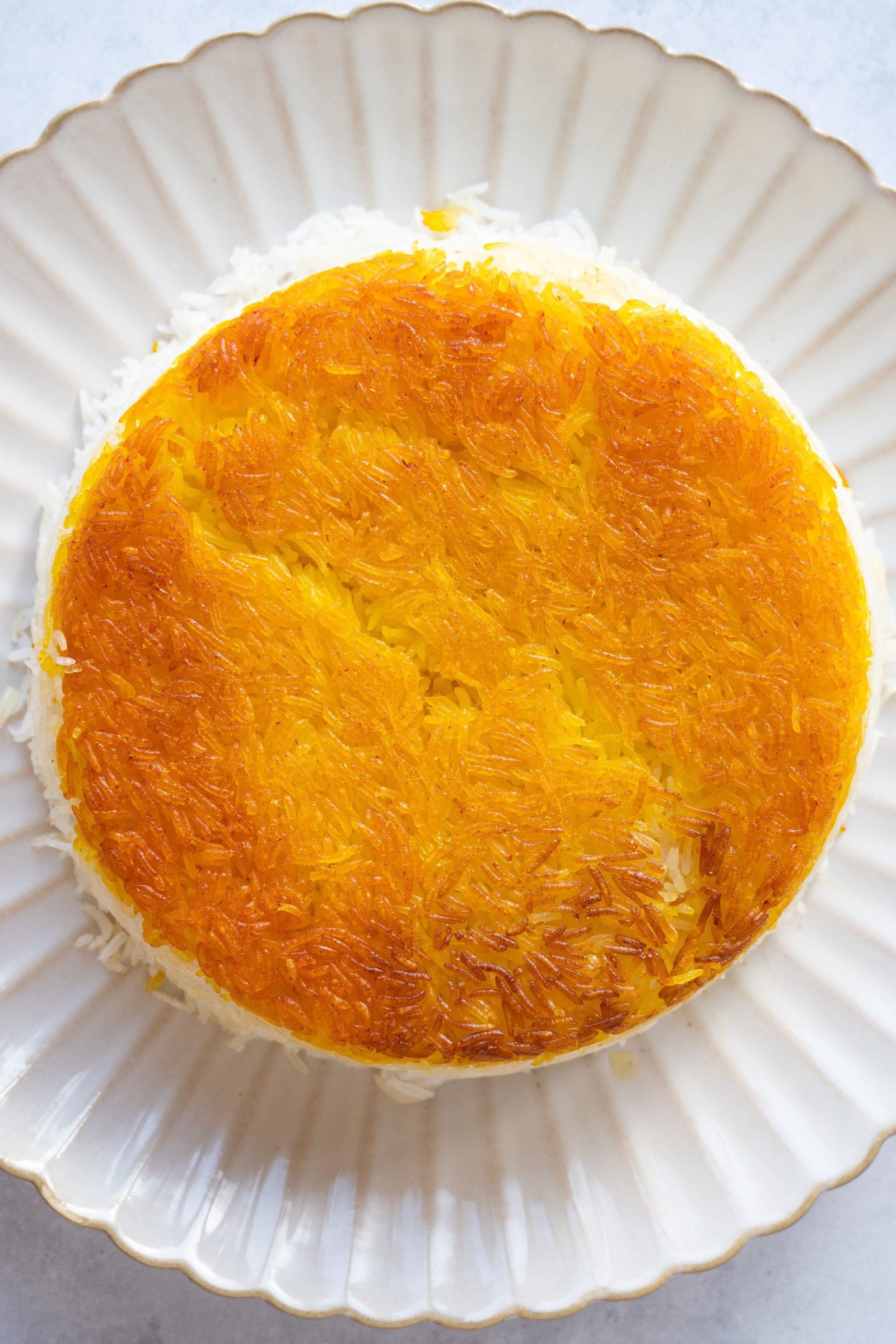 An image of a golden saffron crispy tahdige from the side, showcasing the layers of fluffy rice and crispy crust
