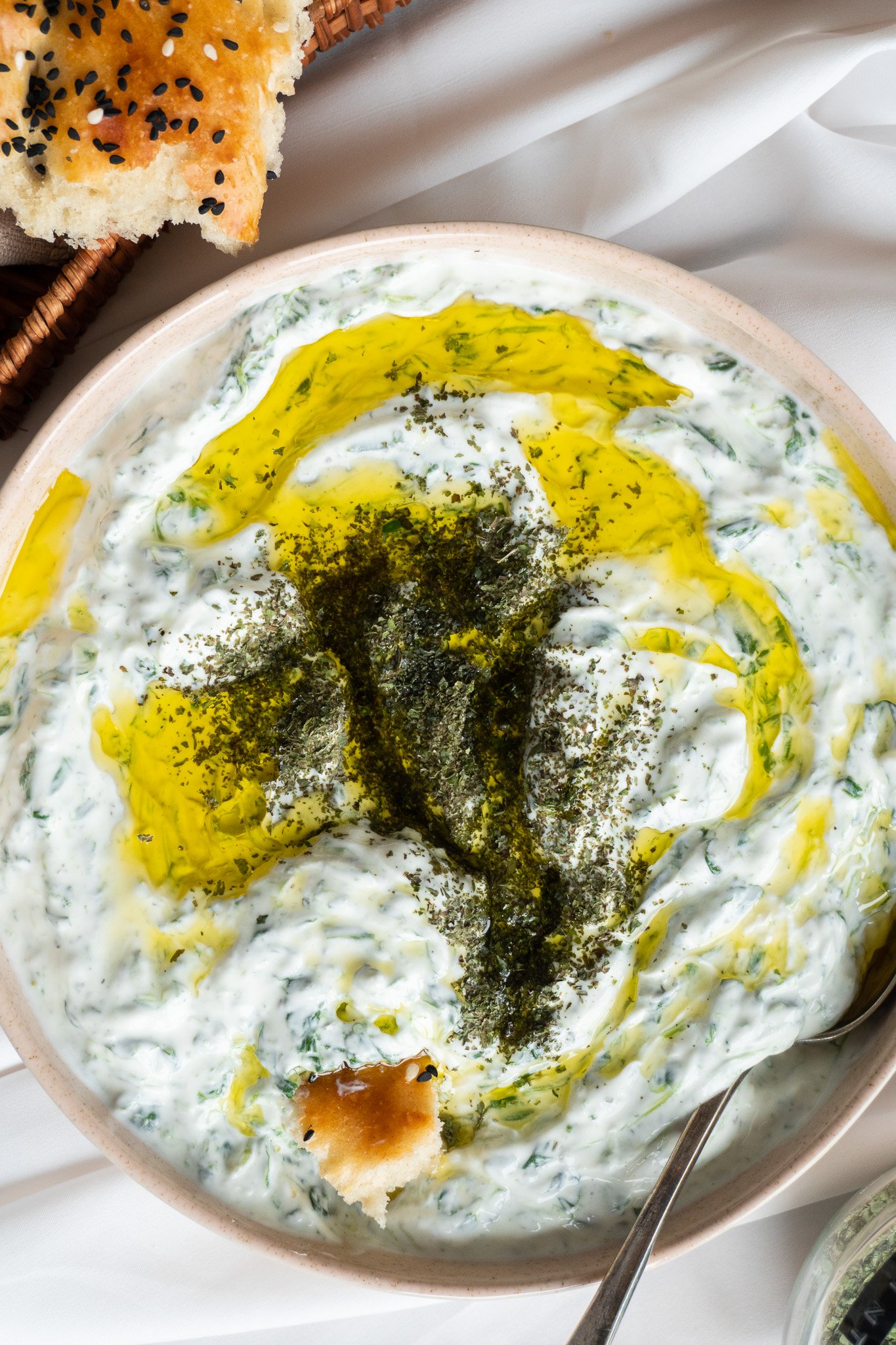 A close-up of Borani Esfenaj, a creamy and refreshing yogurt dip that is popular in Iranian cuisine. The dip is made with spinach, garlic, and is garnished with dried mint leaves.