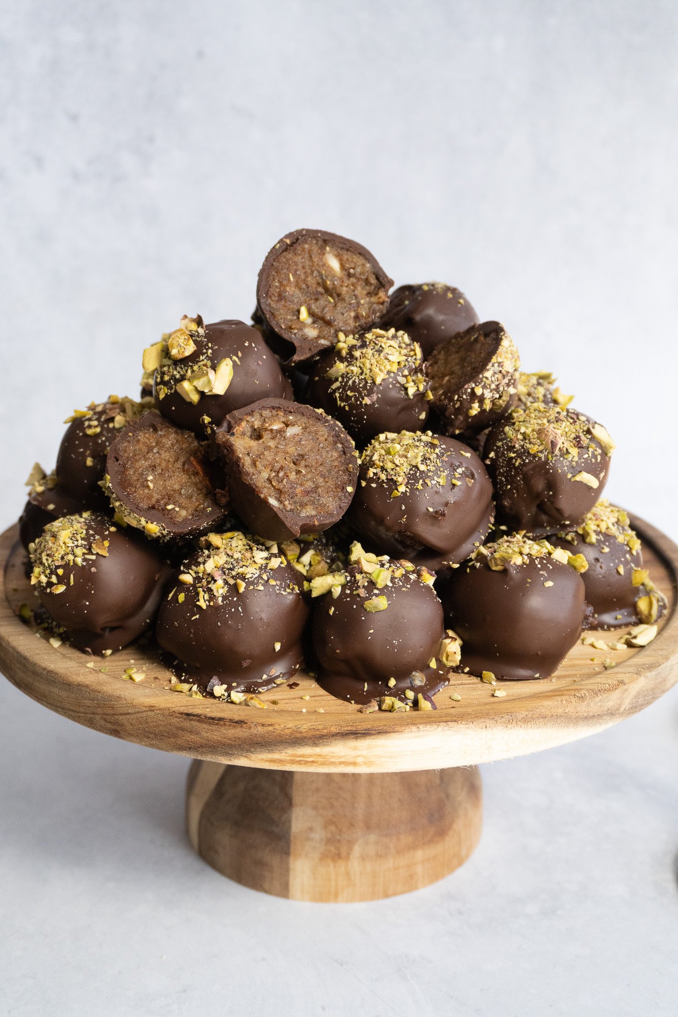 A plate of delicious 10 minute chocolate date truffles coated in chocolate and topped with pistachios.