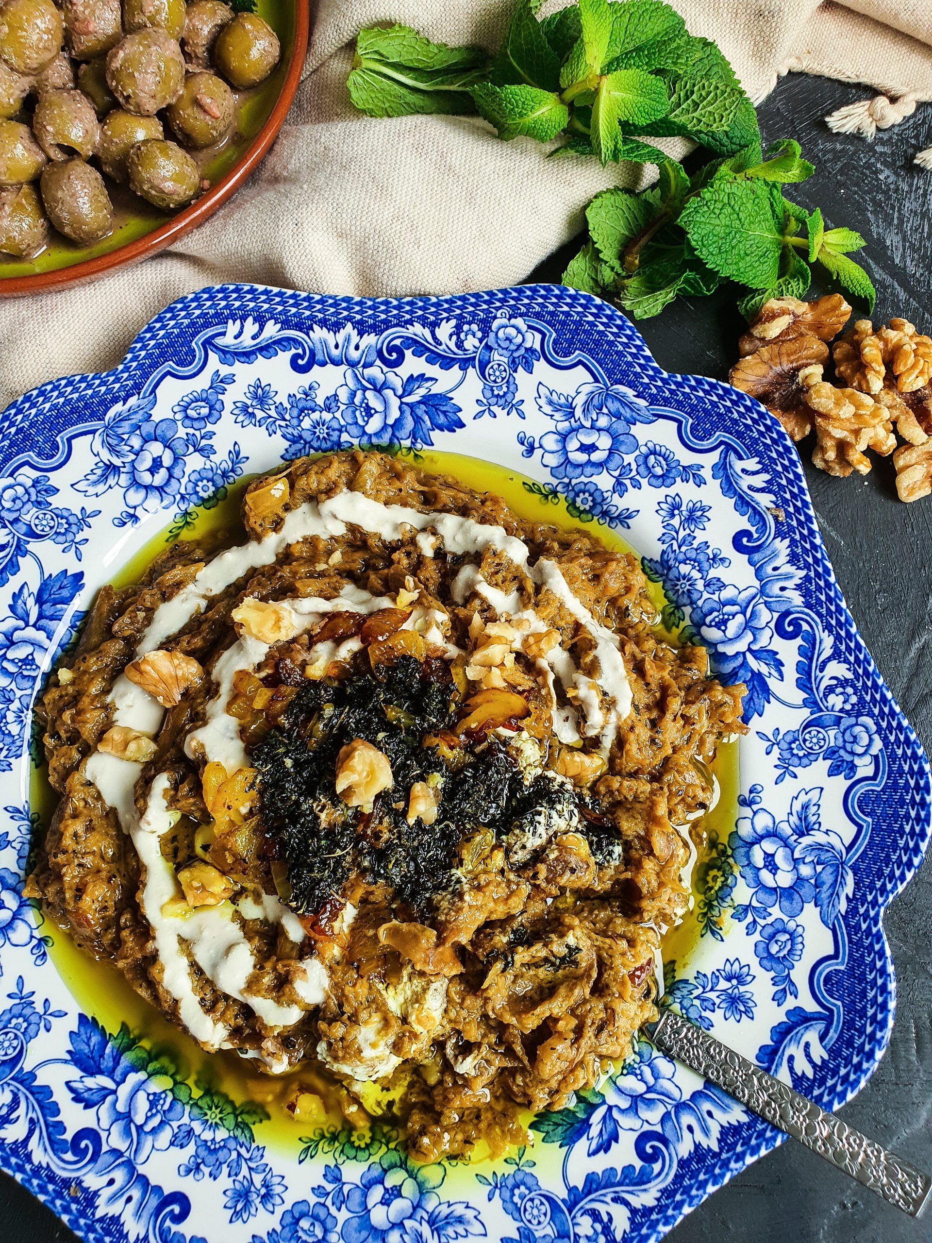 A close-up of a traditional Iranian dish called Kashke Bademjan - persian eggplant dip, consisting of grilled eggplant mixed with whey, garlic, and onion topped with sautéed tomatoes and fried mint leaves.