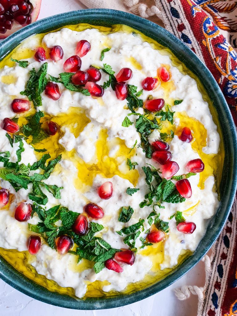 Smoky Creamy Mutabal with Tahini served in a bowl garnished with chopped mint, olive oil and pomegranate seeds. 