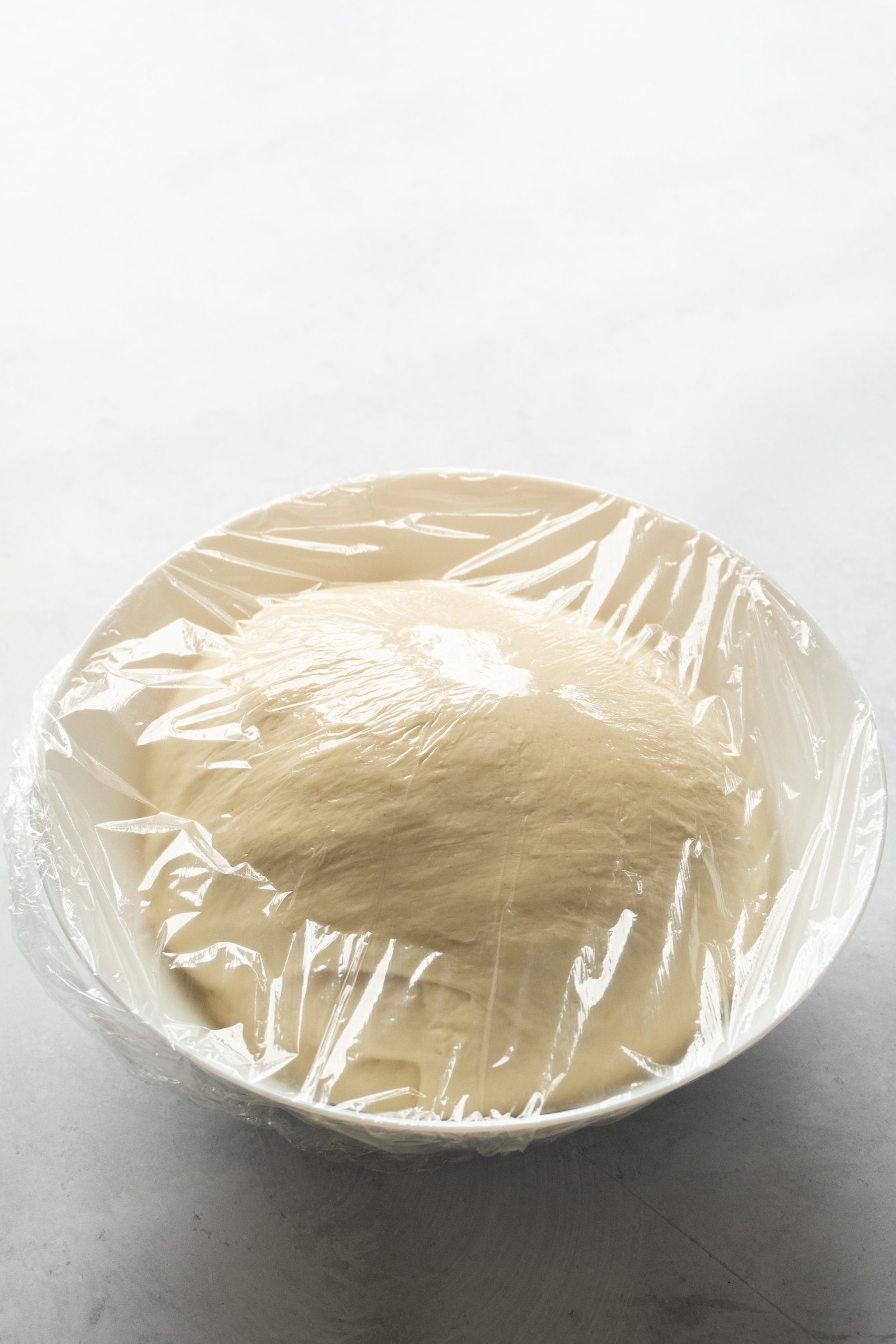 A ball of homemade italian pizza dough resting in a bowl, covered with a cloth, as it rises to its full potential.
