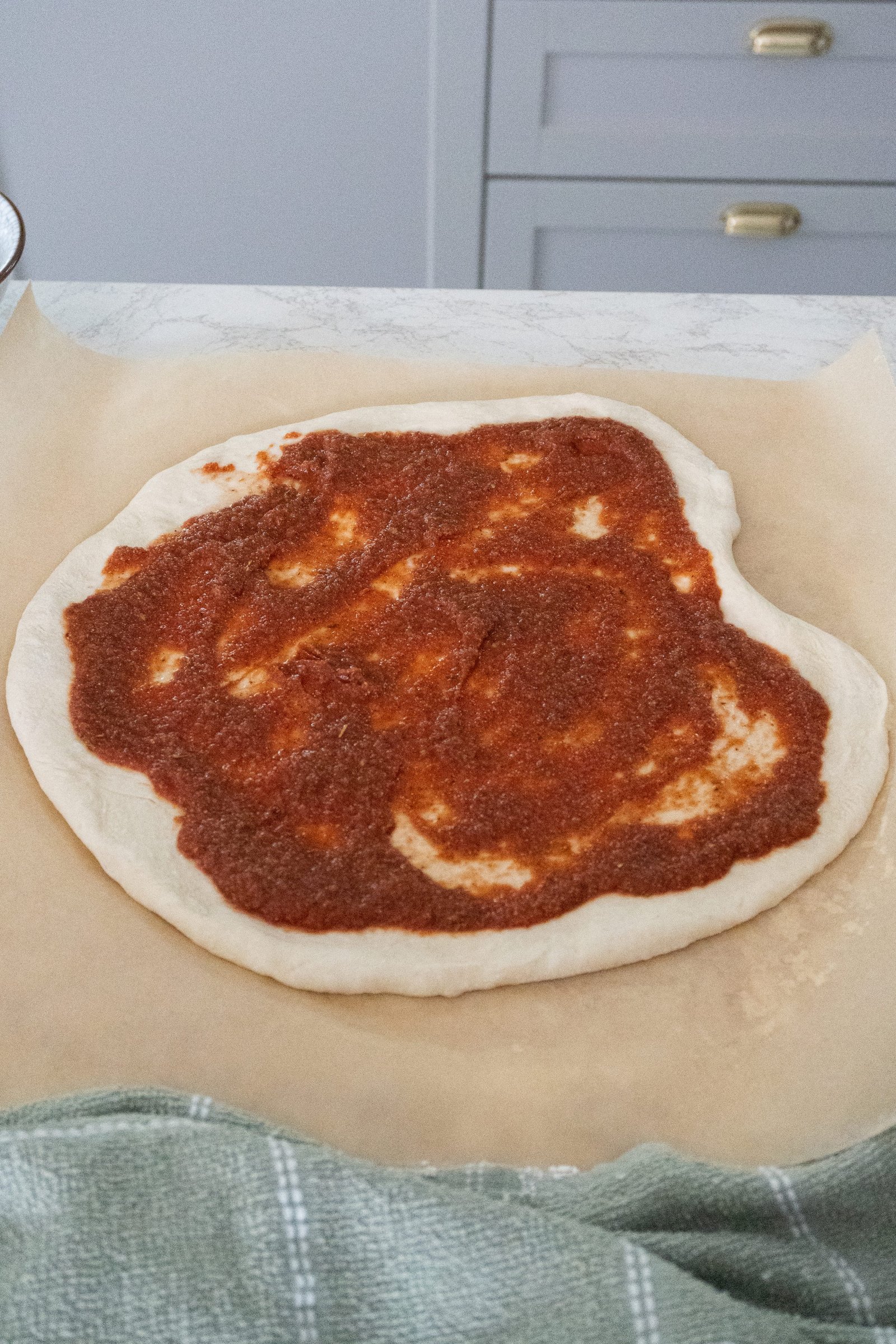 A ball of homemade Italian pizza dough with sauce spread evenly on top, ready to be baked into a delicious, hot, and cheesy pizza.

