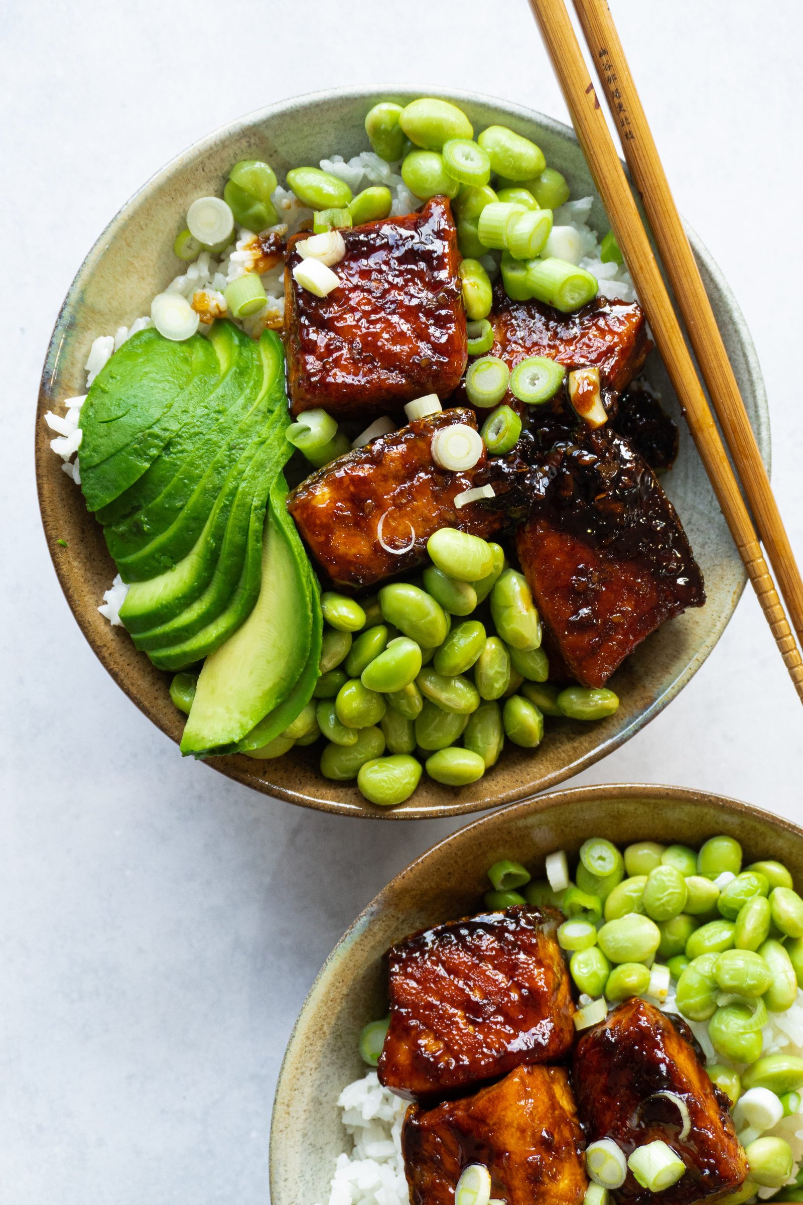 A top-down view of a Crispy Honey Ginger Garlic Salmon Bowl. The dish is served in a white bowl and features a bed of white rice topped with crispy pan-seared salmon, avocado,