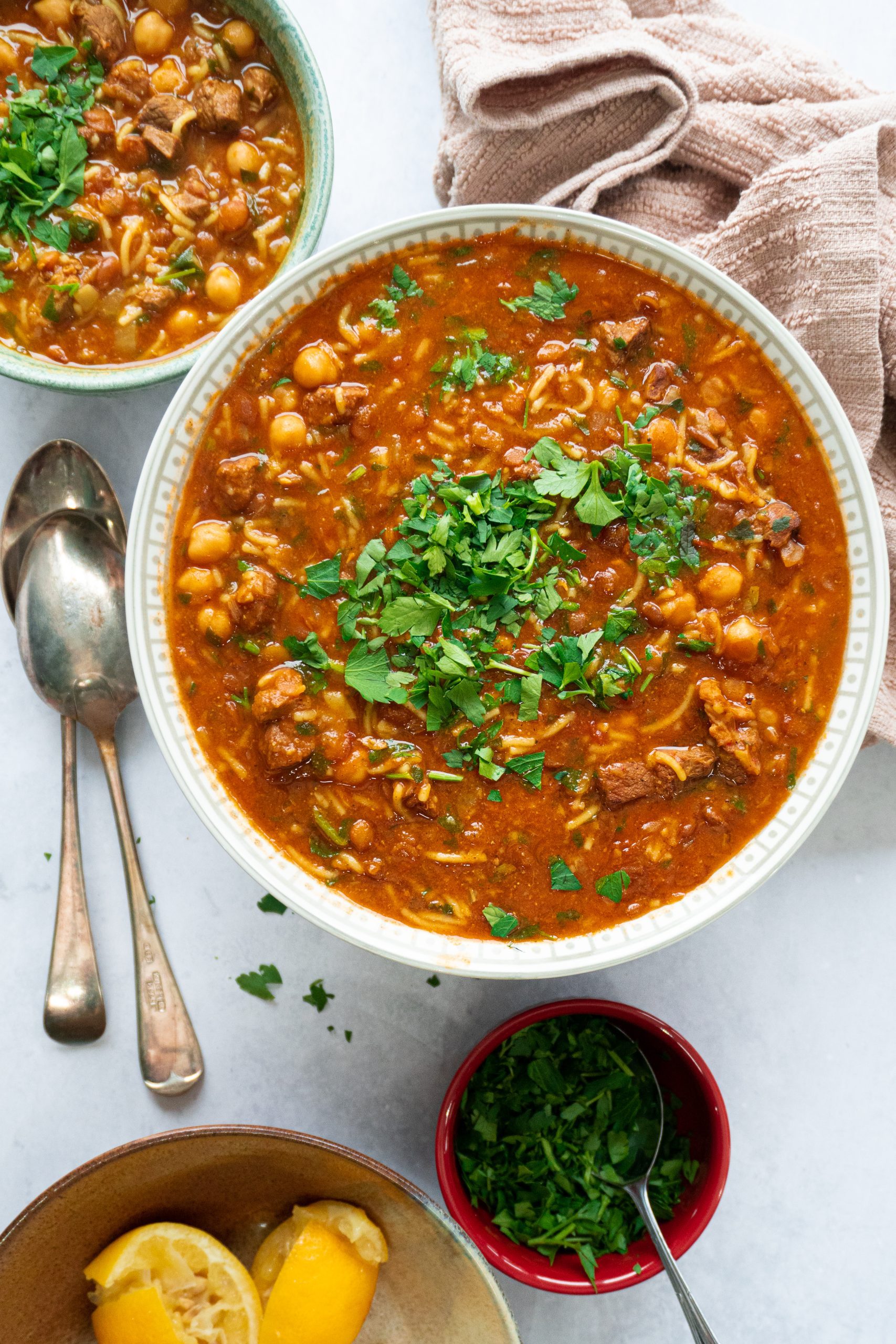 A bowl of steaming hot Authentic Moroccan Harira soup, filled with tender chunks of lamb, lentils, chickpeas, and aromatic spices, garnished with fresh parsley and a squeeze of lemon. A comforting and hearty dish that's perfect for a cold winter's day.