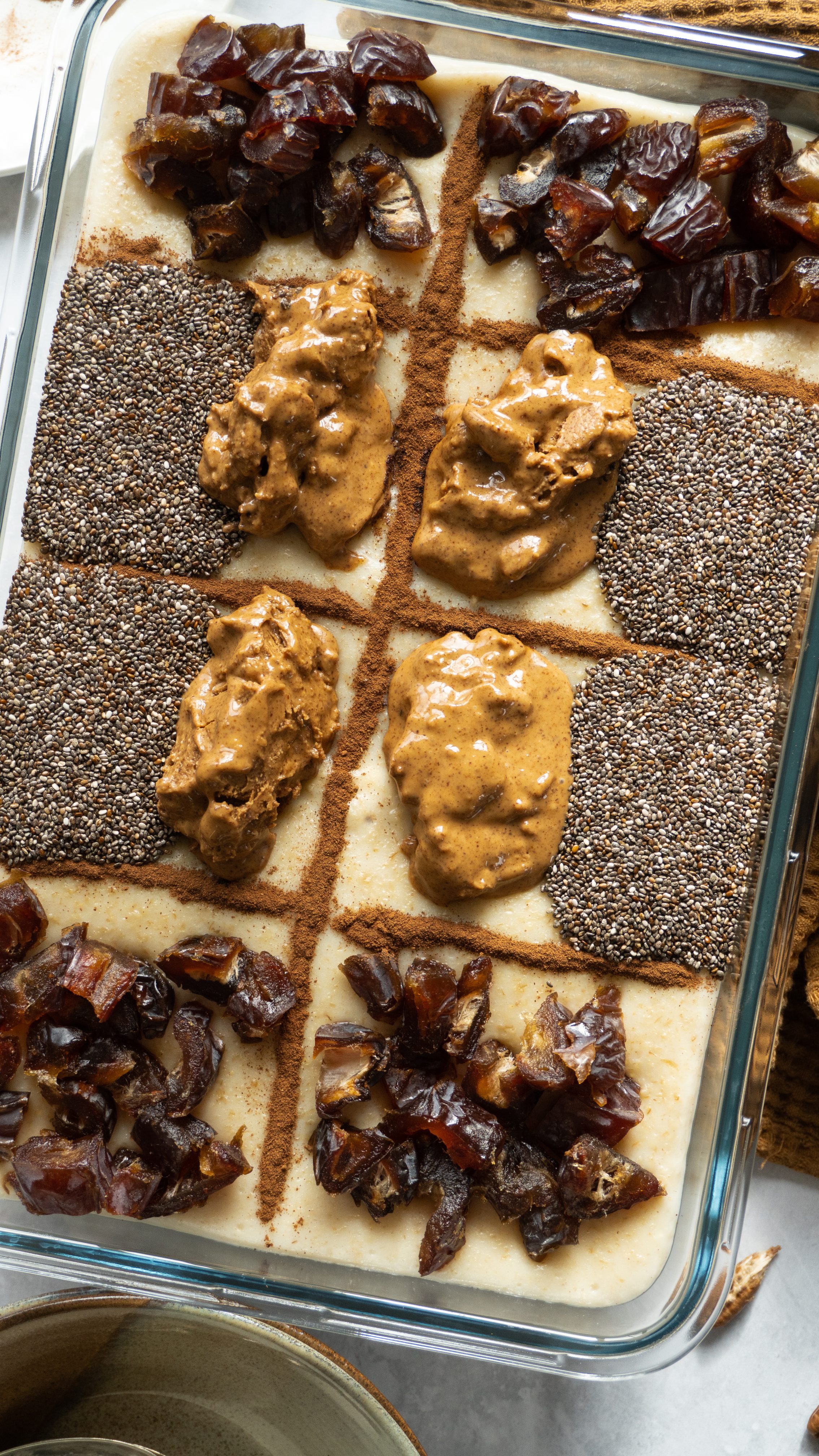 A close-up shot of a steaming dish of cardamom rose date suhoor oatmeal, topped with sliced dates, chopped nuts and seeds, and a sprinkle of cinnamon. The oatmeal is creamy and smooth, with aroma of rose