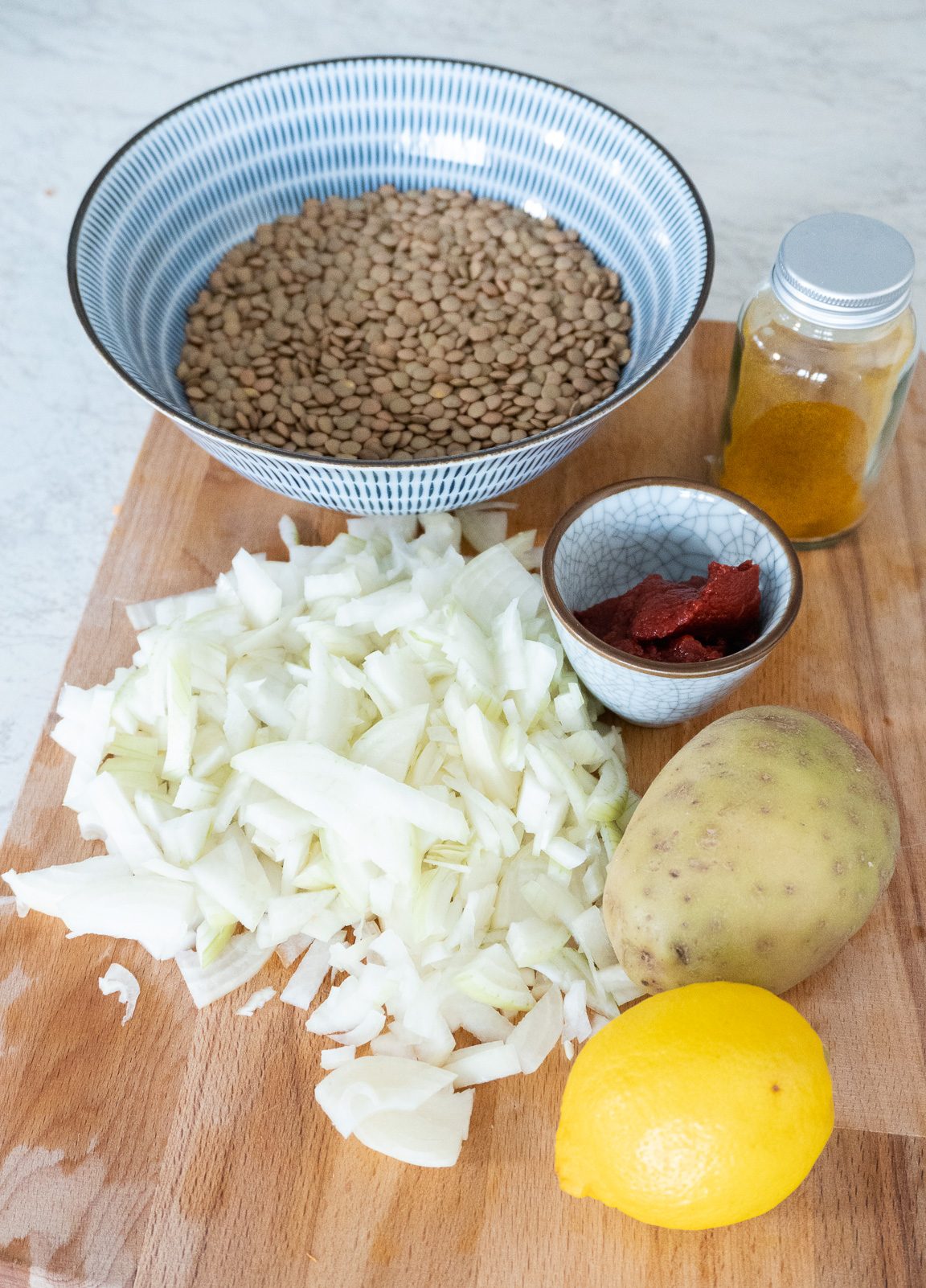 Addasi ingredients on a wooden board, lemon, onions, lentils, tomato puree and potato.