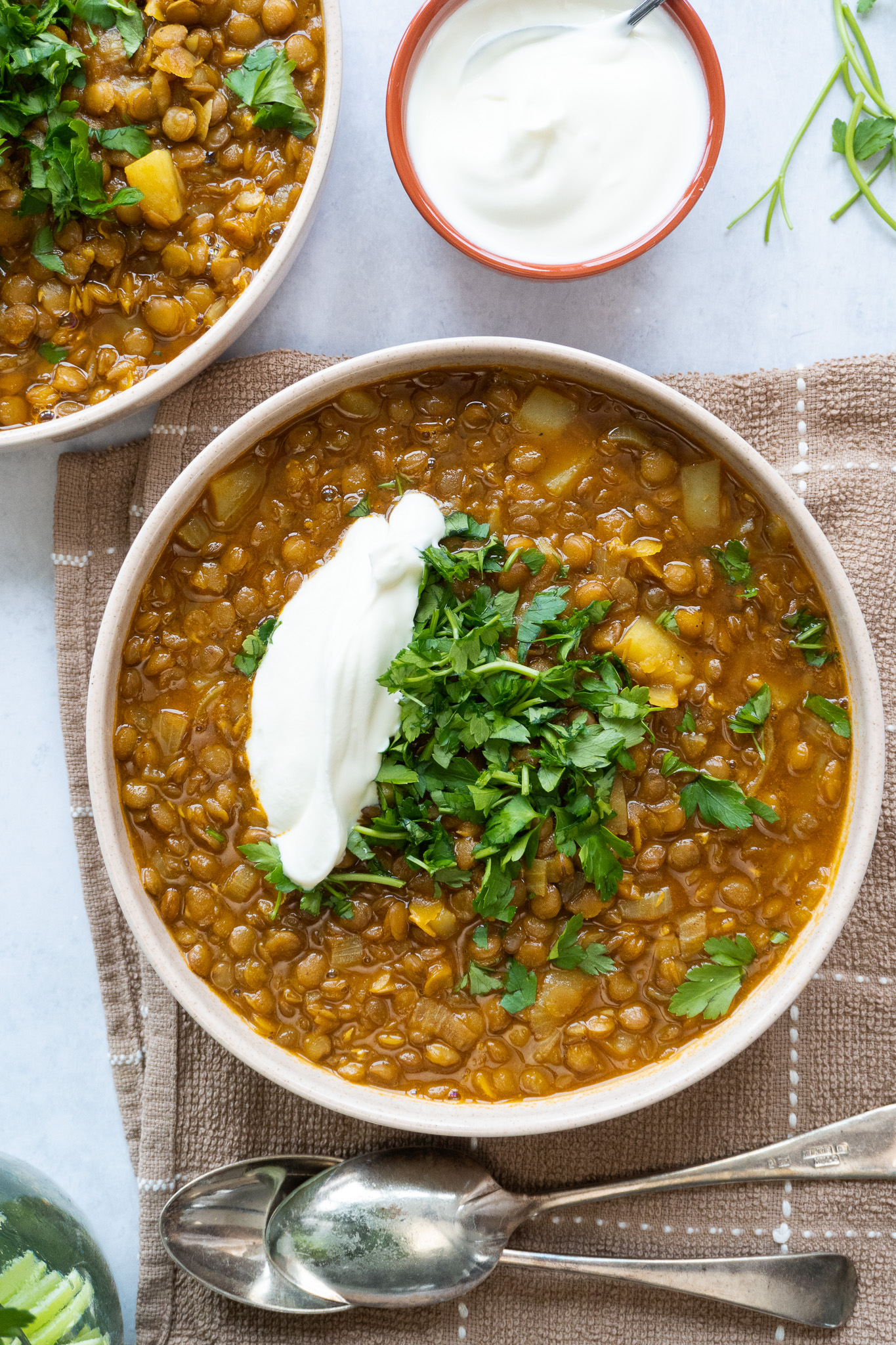 A steaming bowl of Adasi, a flavorful Persian lentil soup, served with a yogurt and topped with chopped herbs. The soup is a warm, comforting mix of lentils, onions, tomatoes, and spices, and is a popular dish in Iranian cuisine.