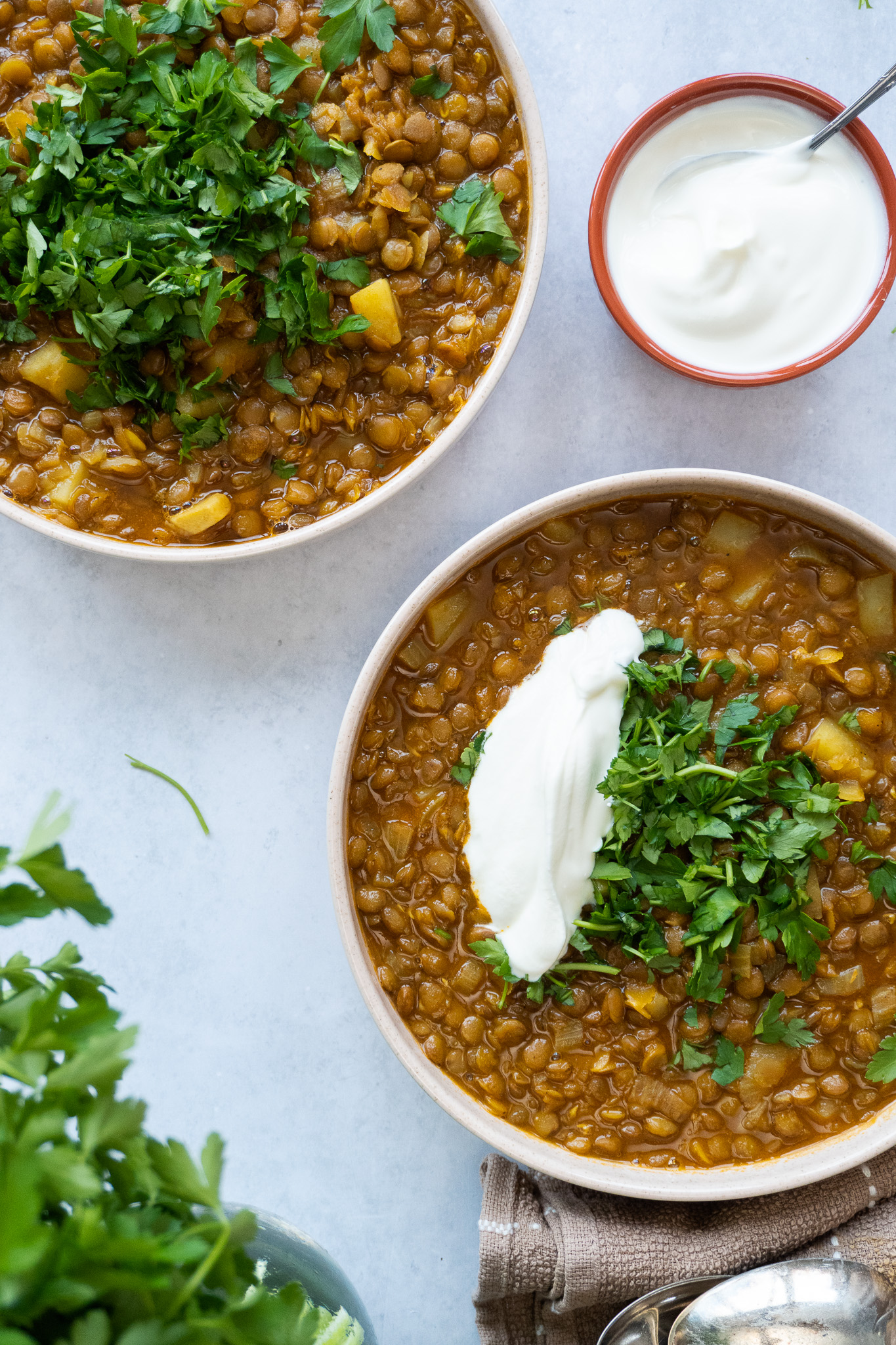 A vibrant image of Adasi Persian Lentil Soup, with a deep reddish-brown color, and decorated with chopped parsley, and a spoonful of yogurt 