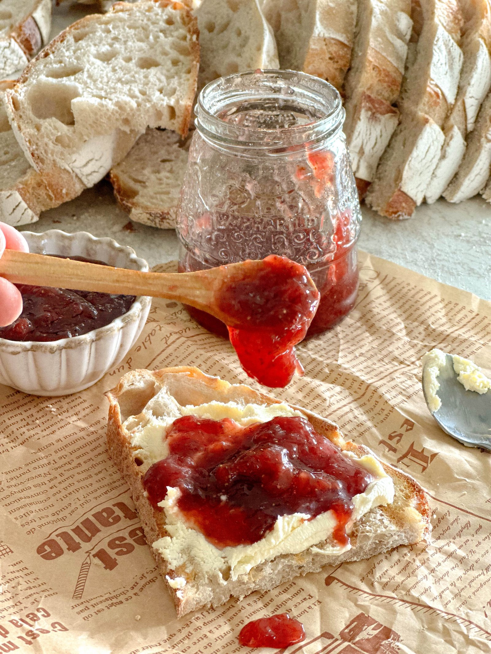 Mama's strawberry jam spread generously on a slice of sourdough toast with clotted cream with this super red jam dripping off the spoon