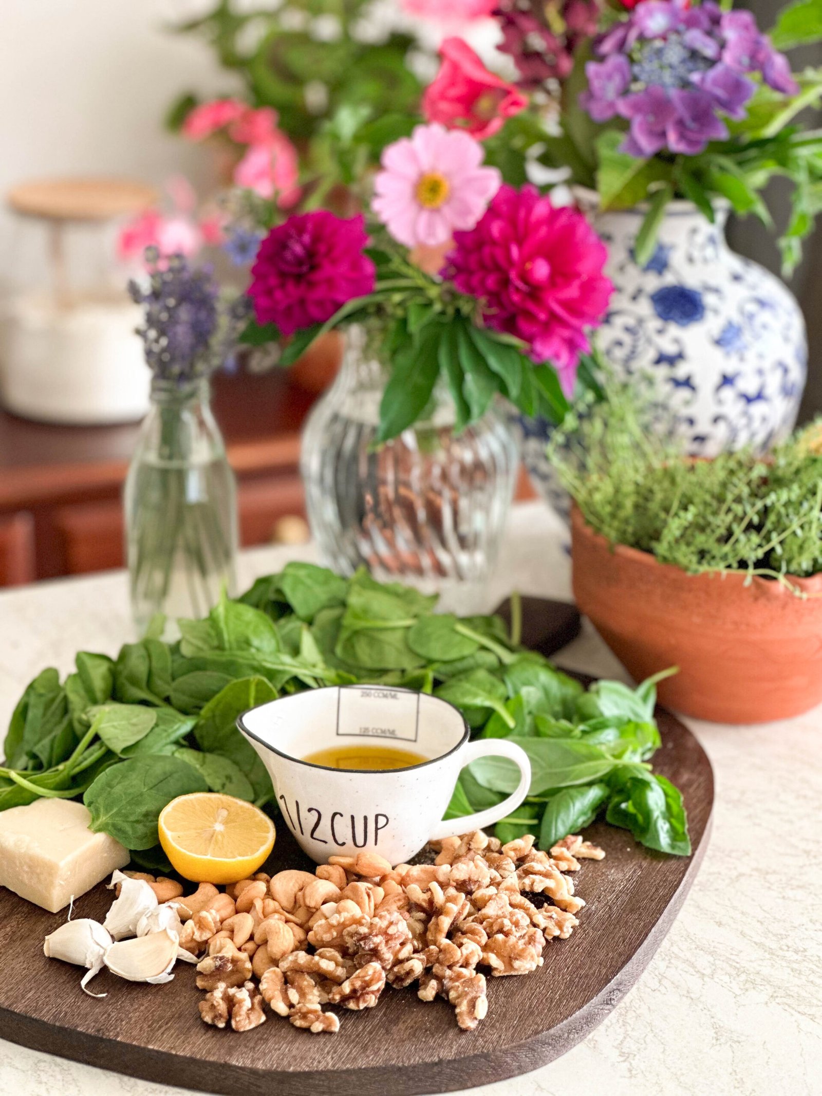 An overhead shot of the ingredients for the pesto pasta salad, including fresh spinach, basil, garlic, Parmesan cheese, cashew nuts, walnuts, lemon, extra-virgin olive oil.