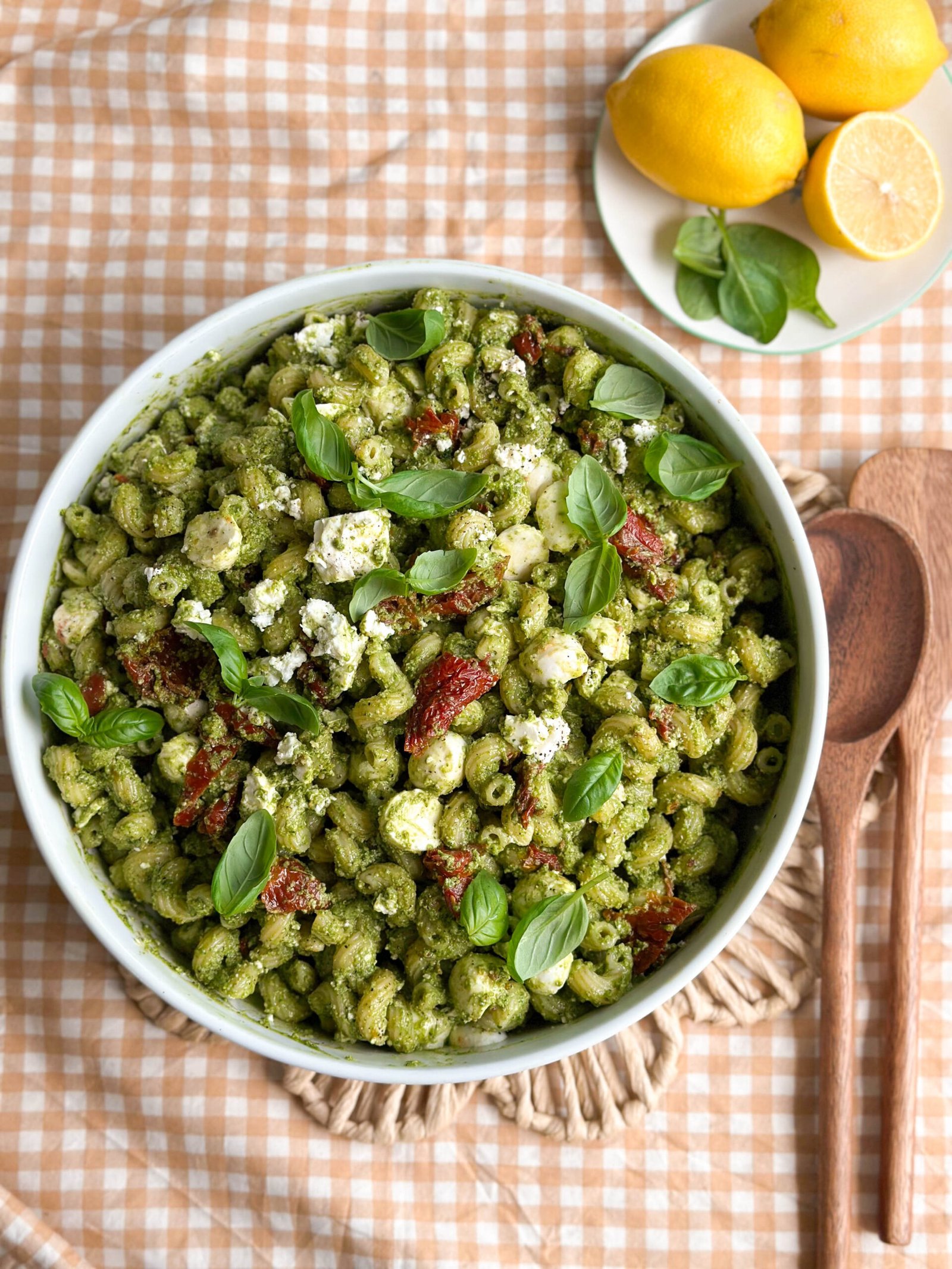 A vibrant bowl of 3 Cheese Spinach Pesto Pasta Salad with sun-dried tomatoes, mozzarella balls, and garnished with fresh basil leaves.