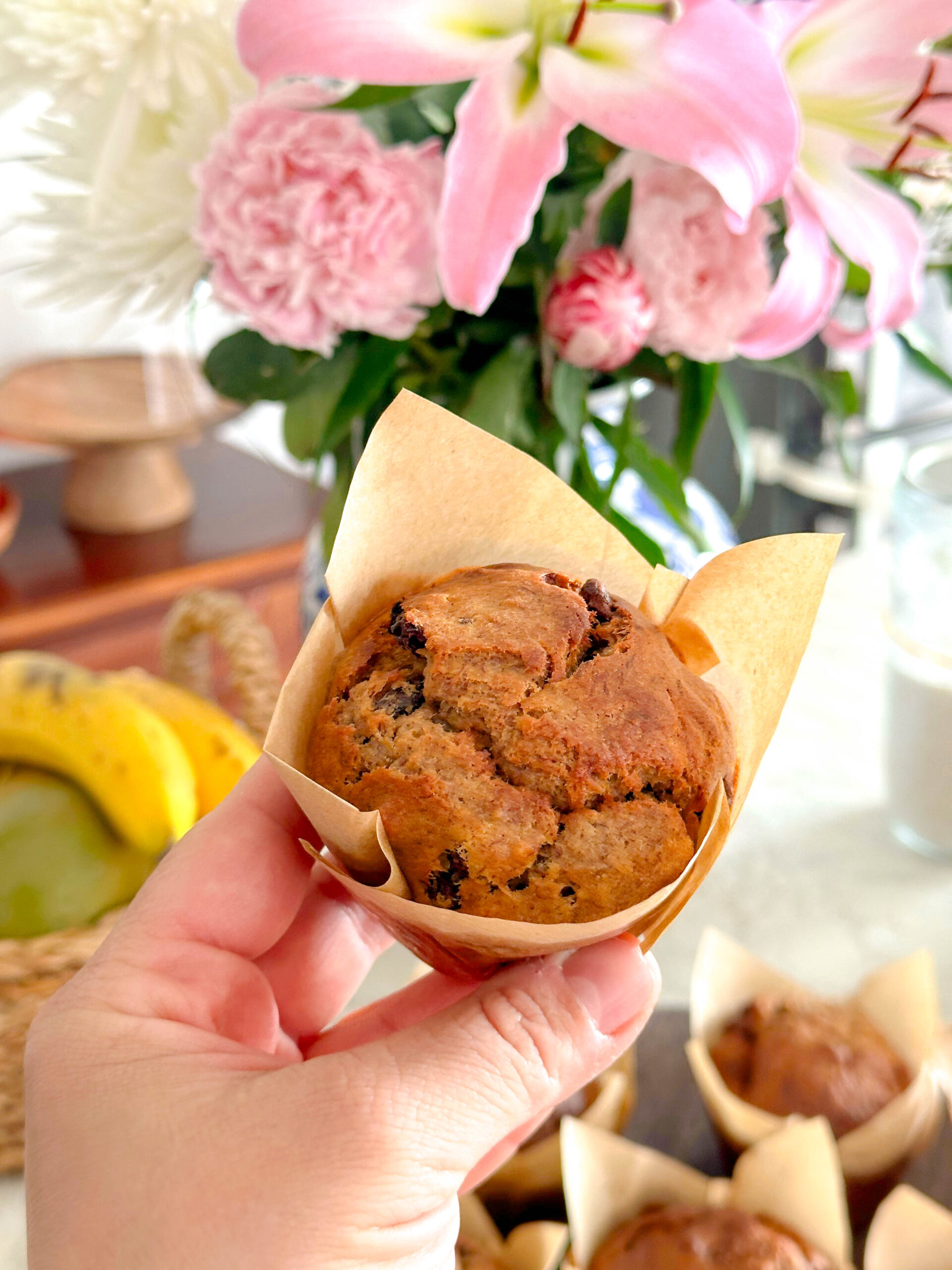 A Sourdough banana bread muffin being help up wrapped in a brown paper muffin case.