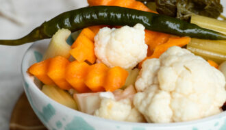 A bowl of Persian Torshi Shoor, ready to eat, with bright pickled red cabbage, orange carrots, green chilies, crunchy cauliflower, and celery sticks glistening in brine.