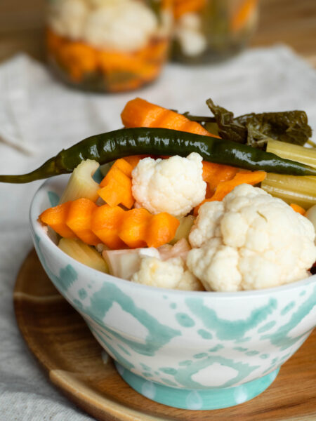 A bowl of Persian Torshi Shoor, ready to eat, with bright pickled red cabbage, orange carrots, green chilies, crunchy cauliflower, and celery sticks glistening in brine.