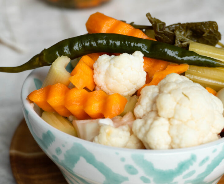 A bowl of Persian Torshi Shoor, ready to eat, with bright pickled red cabbage, orange carrots, green chilies, crunchy cauliflower, and celery sticks glistening in brine.