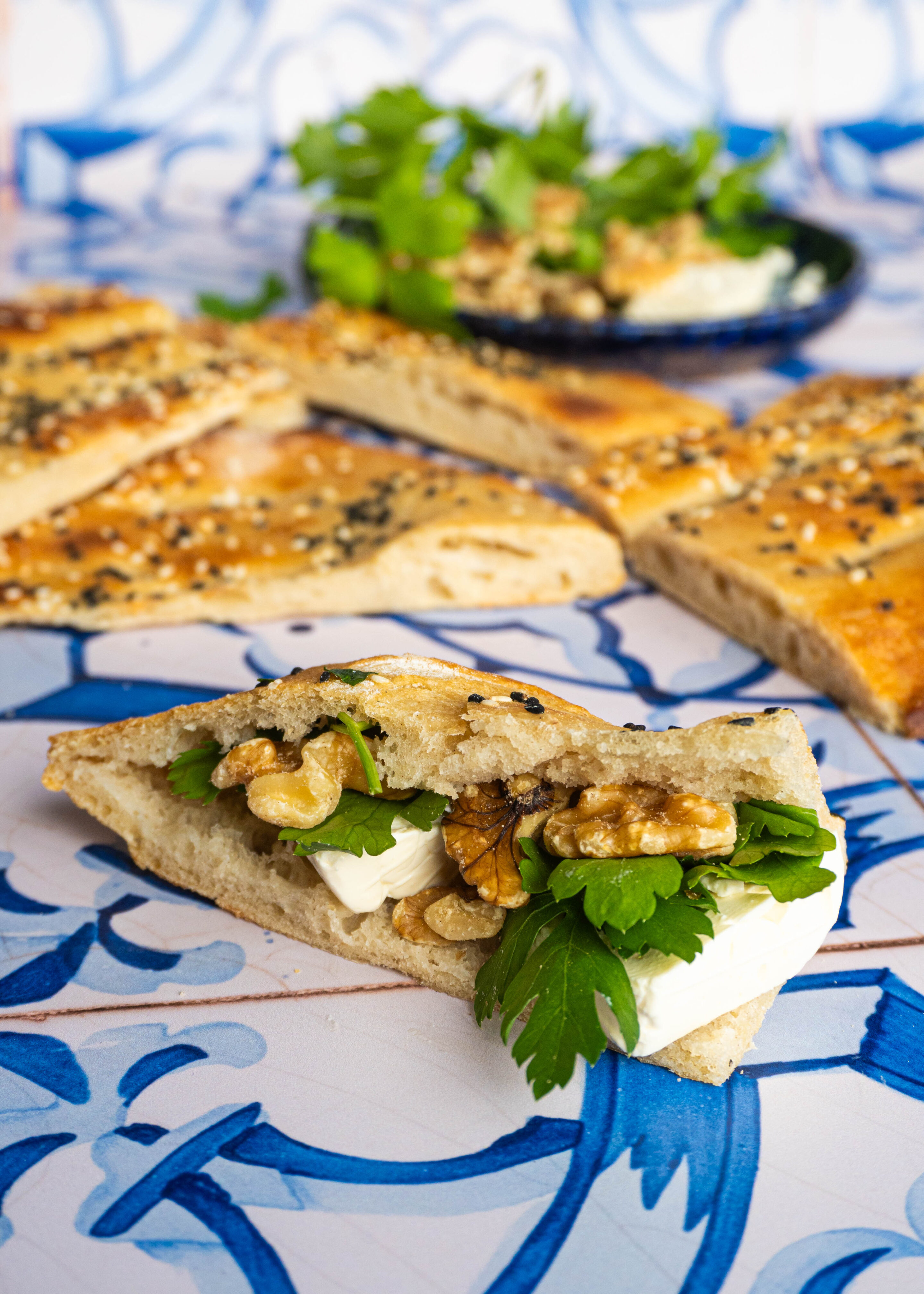 A single bite of Barbari bread, filled with feta cheese, crunchy walnuts, and vibrant fresh herbs, held up ready to be devoured — a true Persian breakfast moment.