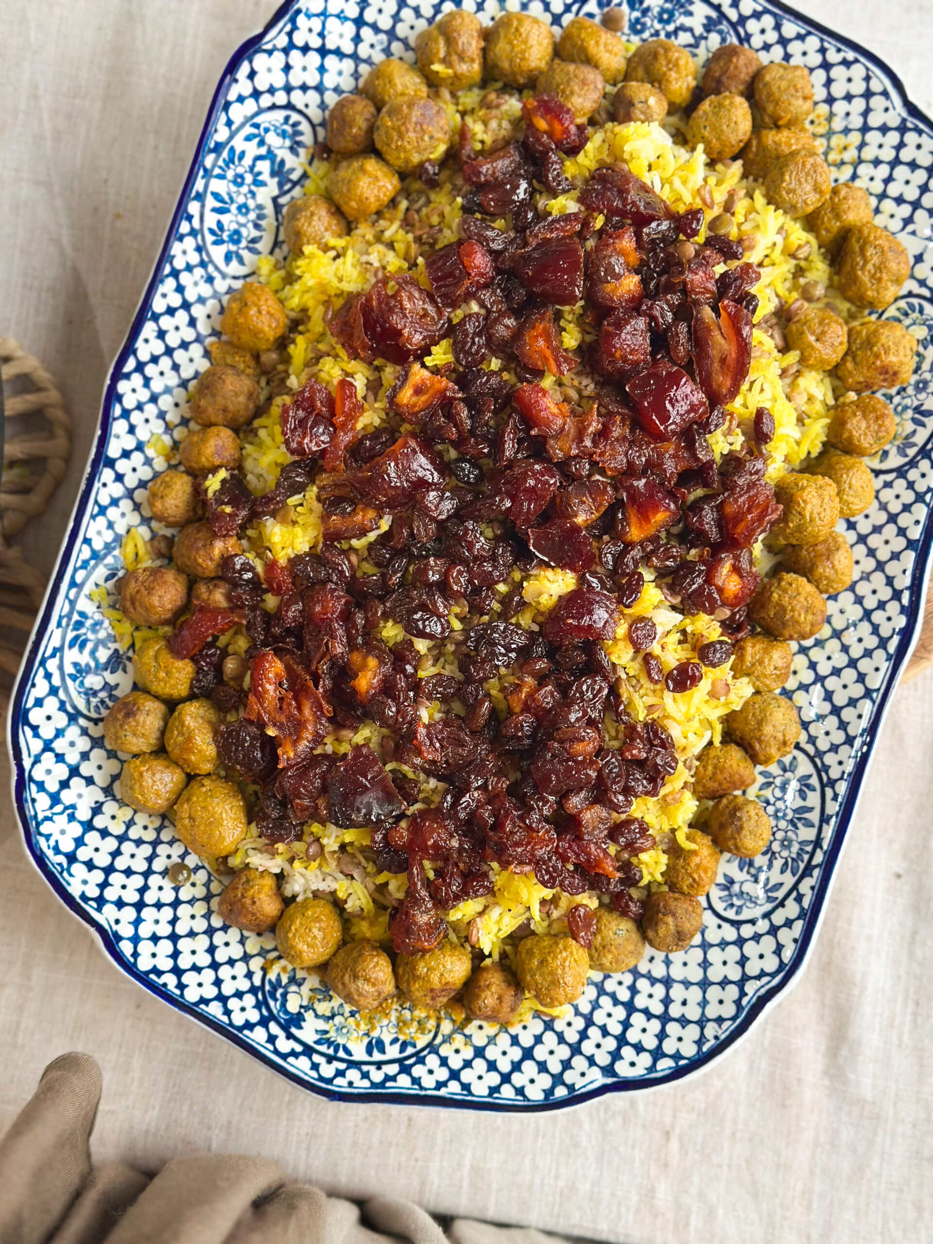 Close-up of Adas Polo, Persian lentil rice topped with spiced meatballs, caramelised dates, and sultanas, served on a rustic platter.