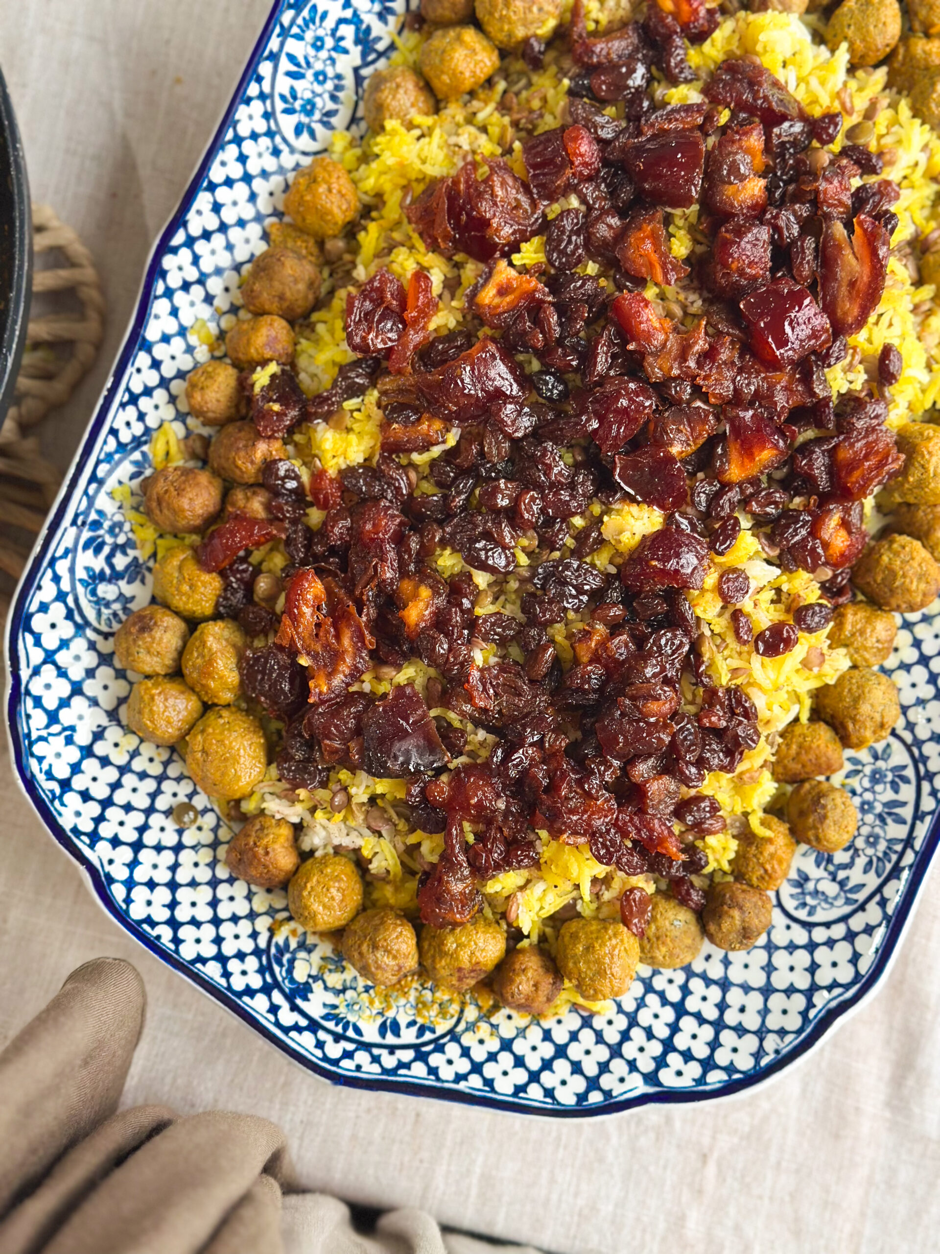 Close-up of Adas Polo, Persian lentil rice topped with spiced meatballs, caramelised dates, and sultanas, served on a rustic platter.