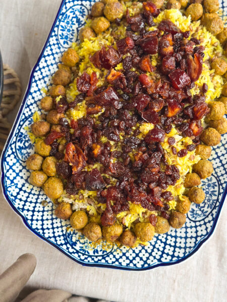 Close-up of Adas Polo, Persian lentil rice topped with spiced meatballs, caramelised dates, and sultanas, served on a rustic platter.