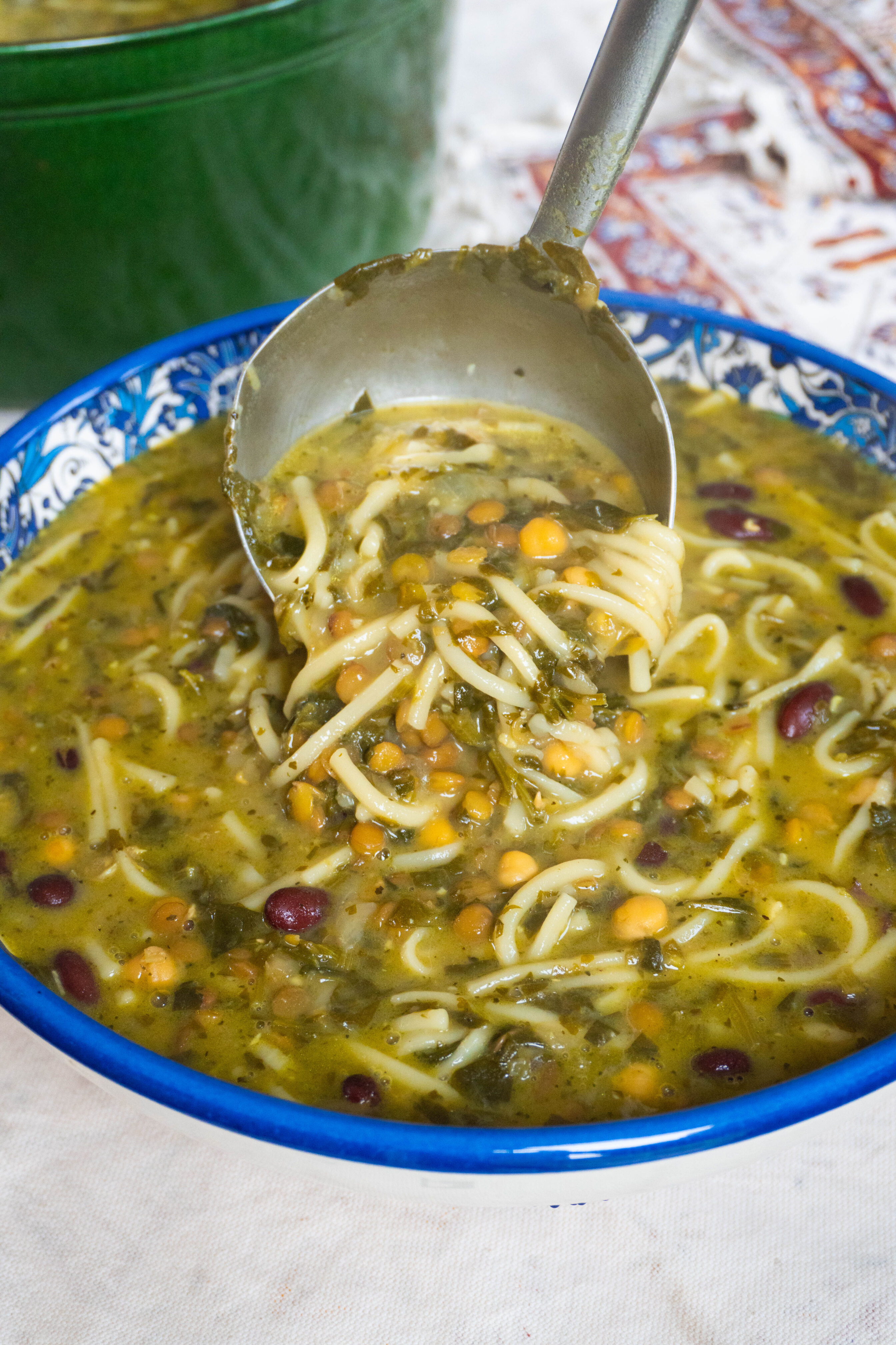 Savor the rich flavors of Ashe-Reshteh, a Persian noodle soup made with lentils, chickpeas, and fresh herbs, topped with fried onions, sautéed mint, and creamy Kashk.