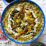 A bowl of Delicious Ashe-Reshteh, a traditional Persian noodle soup with lentils, chickpeas, kidney beans, and fresh herbs, topped with fried onions, mint, and a touch of Kashk.