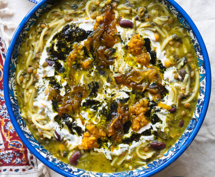 A bowl of Delicious Ashe-Reshteh, a traditional Persian noodle soup with lentils, chickpeas, kidney beans, and fresh herbs, topped with fried onions, mint, and a touch of Kashk.