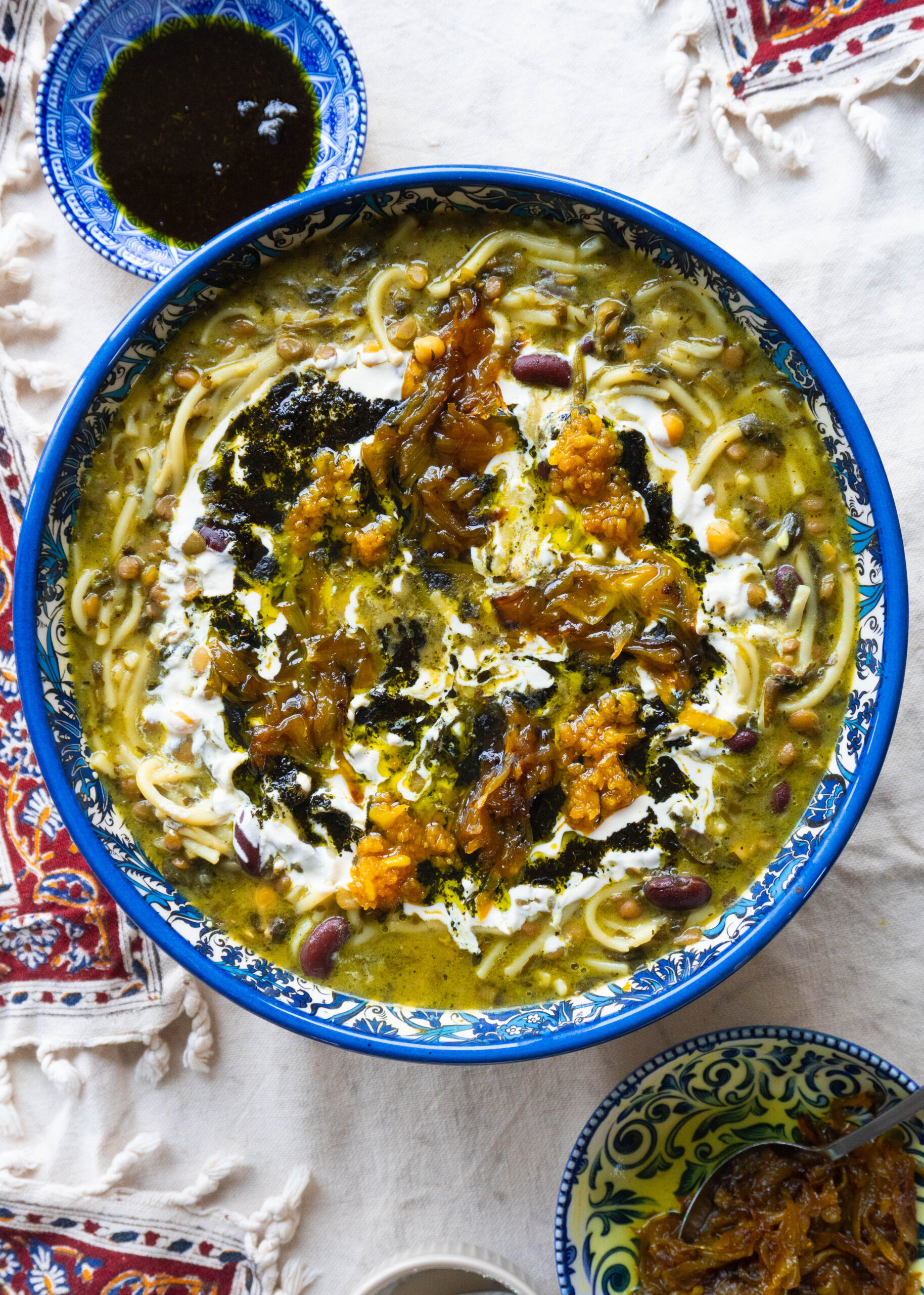 A bowl of Delicious Ashe-Reshteh, a traditional Persian noodle soup with lentils, chickpeas, kidney beans, and fresh herbs, topped with fried onions, mint, and a touch of Kashk.