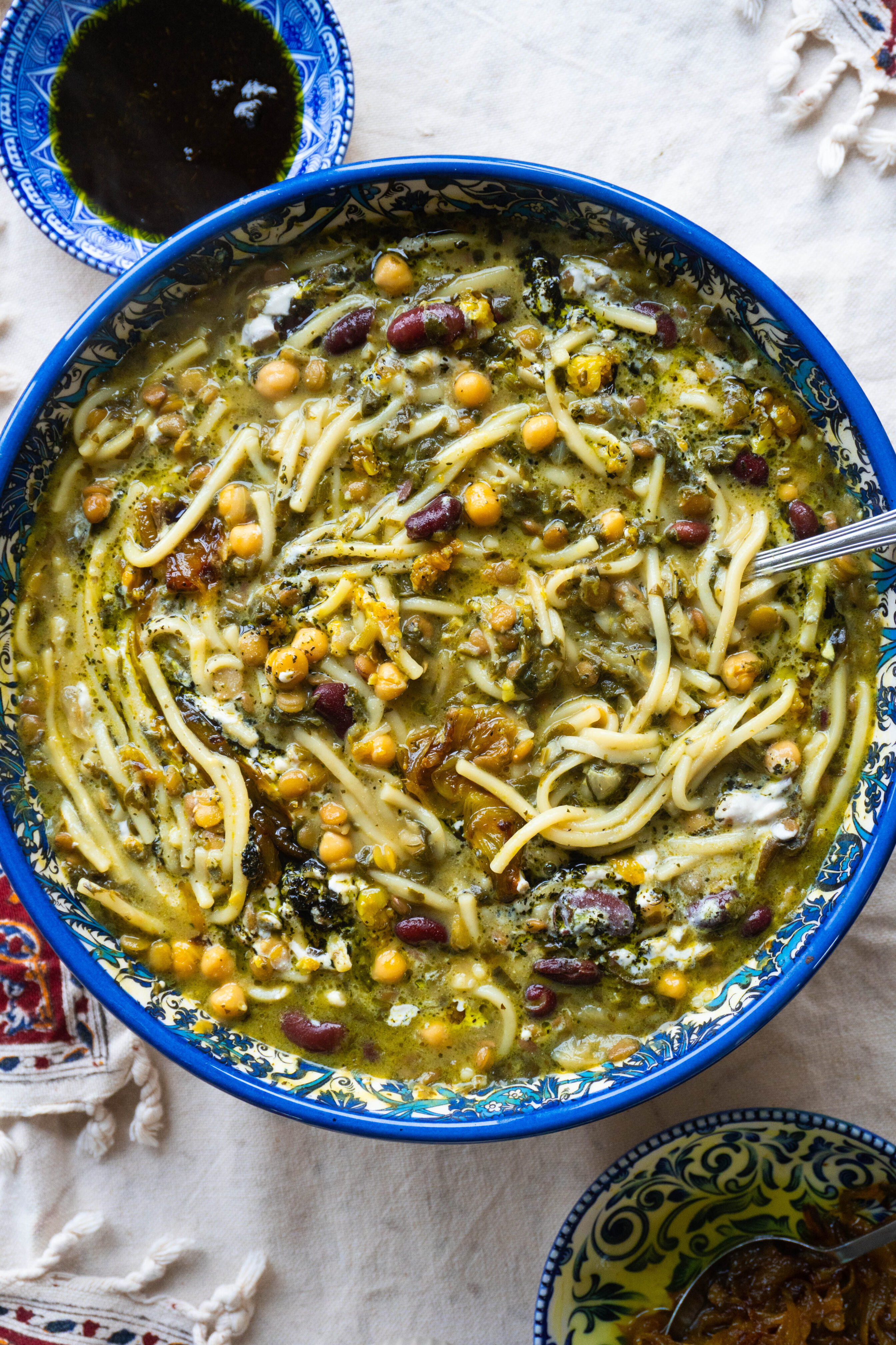 Hearty and flavourful Ashe-Reshteh, a Persian noodle soup filled with legumes, greens, and savory spices, finished with a garnish of crispy onions and fresh mint.